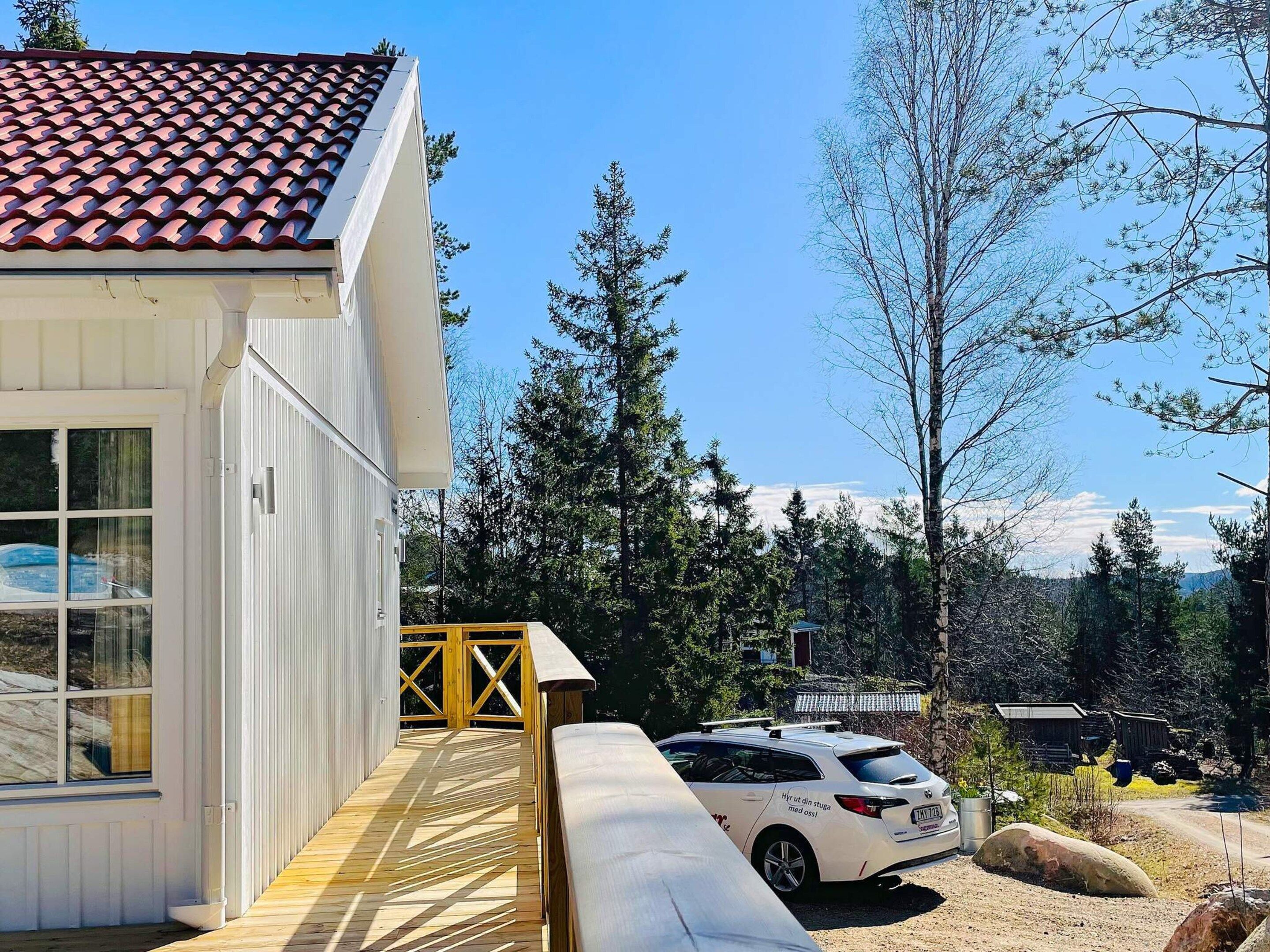 A white building with a tiled roof, a wooden deck, and a parked car.