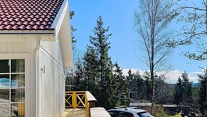 Ein weißes Gebäude mit einem Ziegeldach, einer Holzdachterrasse und einem parkenden Auto.