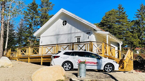 Ein weißes Gebäude mit einer Holzterrasse und einem geparkten Auto davor.