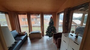 Ett mysigt vardagsrum med en soffa, ett litet bord, en julgran och ett fönster med utsikt över en trädgård.