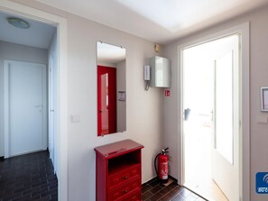 A hallway with a red fire extinguisher, a white door, and a red cabinet. - Parkhouse B201 Cosy Apartment in De Haan (De Haan)