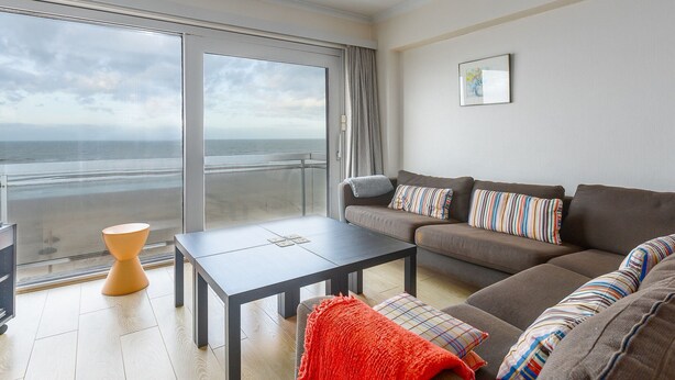A modern living room with a large window overlooking the sea, a sofa set, a coffee table, and a small orange side table. - Retreat With Pool Access (Middelkerke)