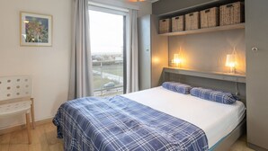 A bedroom with a bed, a desk, a chair, a window with curtains, and a city view. - Retreat With Pool Access (Middelkerke)