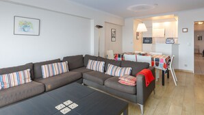 A modern living room with a sofa, coffee table, and a dining area with a table and chairs. - Retreat With Pool Access (Middelkerke)