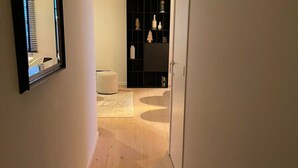 Ein Flur mit Holzboden, einem weißen Stuhl und einem schwarzen Regal mit Dekorationen.
