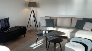 Ein modernes Wohnzimmer mit einer Couch, zwei runden Tischen, einer Stehlampe und einem Fernseher auf einem schwarzen Lowboard.