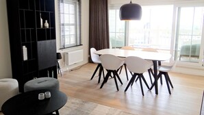 Ein modernes Wohnzimmer mit Essbereich, ausgestattet mit einer schwarzen Unterhaltungsanlage, einem runden Couchtisch und einem großen Fenster mit Vorhängen.