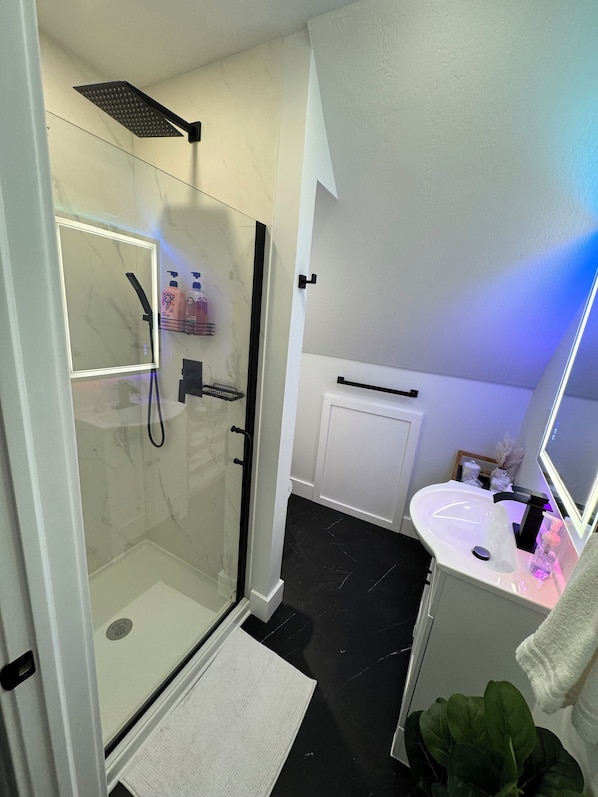 A modern bathroom with a glass-enclosed shower, a white sink with a mirror, and a black tiled floor.