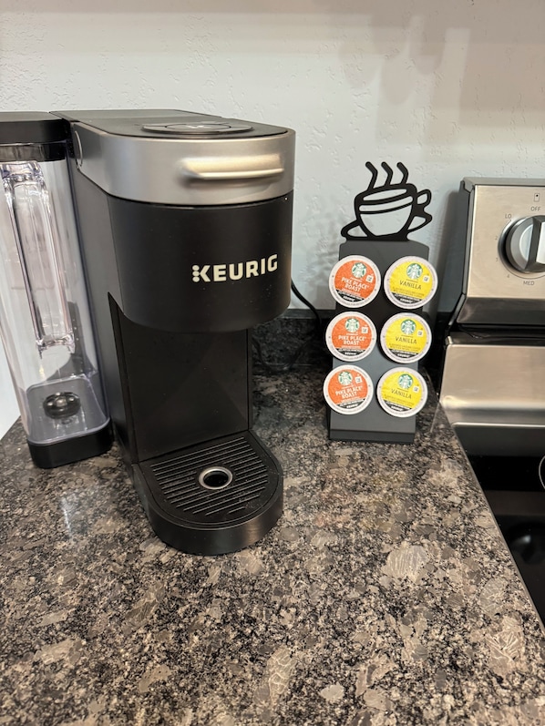 Eine Keurig-Kaffeemaschine steht auf einer Granitabdeckung, zusammen mit einem Vorratshalter für Kaffeekapseln, der mehrere Kapseln enthält.