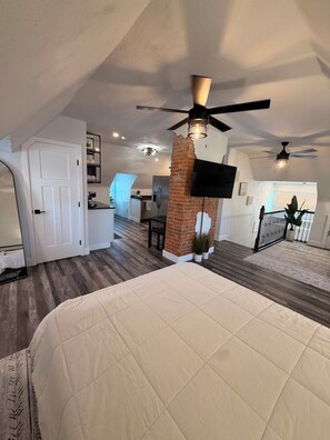 A spacious loft bedroom with a large bed, a brick accent wall, a ceiling fan, and a TV mounted on the wall. - One of the oldest houses in Butler, with an updated vibe. (Butler)