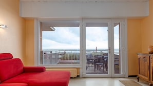 Ein Zimmer mit einem roten Sofa, einem Holzschrank und Meerblick durch eine Glastür.