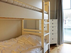 Un lit superposé avec un espace de rangement en dessous, une fenêtre avec des rideaux et une vue sur un bâtiment à l’extérieur.