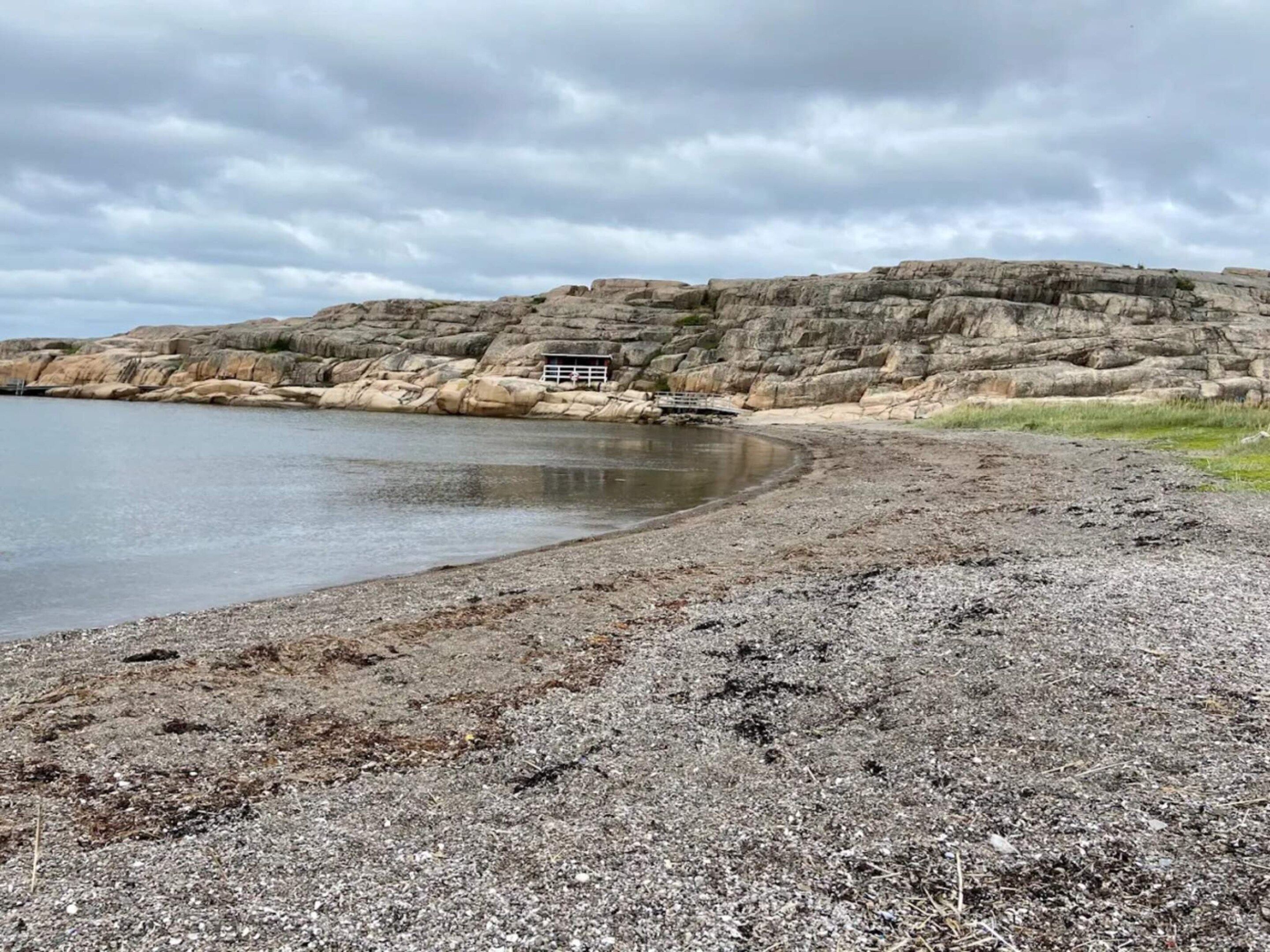 Une plage rocheuse avec une petite construction, peut-être un abri, près de l’eau.