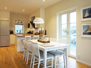 Une cuisine moderne avec des meubles blancs, un coin repas comprenant une table et des chaises blanches, et une grande fenêtre donnant sur la mer.