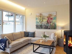 Een moderne woonkamer met een hoekbank, een salontafel, een open haard en een groot abstract schilderij aan de muur.