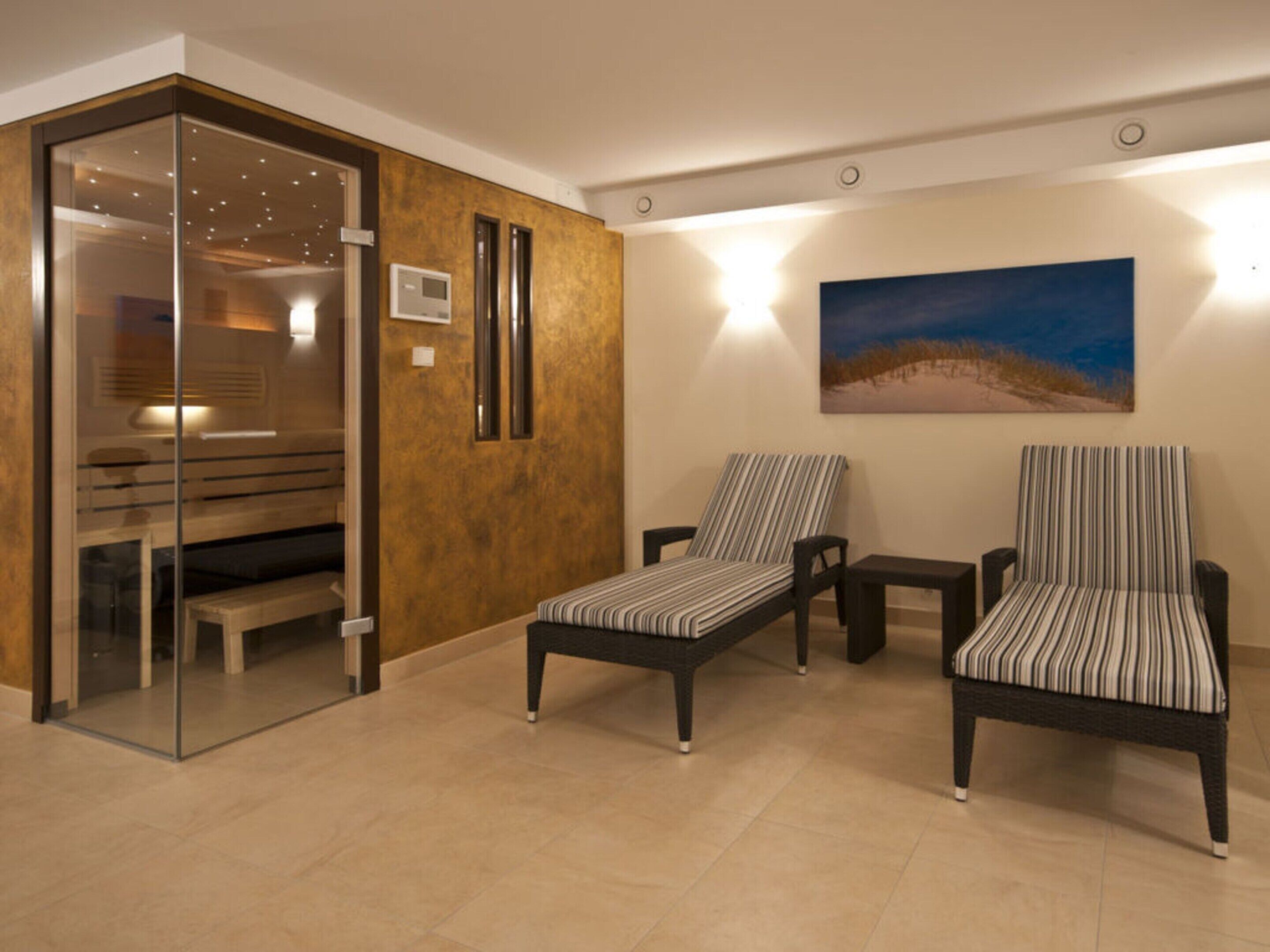A modern lobby with a glass door leading to a room, two striped armchairs, a small table, and a painting of a beach scene.