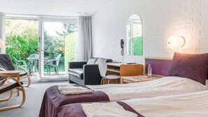 A hotel room with two beds, a desk, a chair, and a view of greenery outside. - Holiday Home With Nature Access (Nexø)