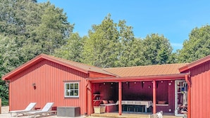 A red wooden house with a covered patio, a hot tub, and a deck with lounge chairs. - 6 Person Holiday Home in Ljungby (Ljungby)