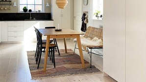 A modern kitchen with white cabinets, a wooden dining table, and a woven rug. - 6 Person Holiday Home in Ljungby (Ljungby)