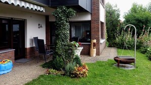 A two-story house with a balcony, a garden with a grill, and a chair outside.