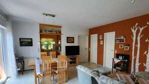 Un soggiorno moderno con un divano grigio, un tavolo da pranzo in legno e sedie. Sullo sfondo, una televisione e una libreria.