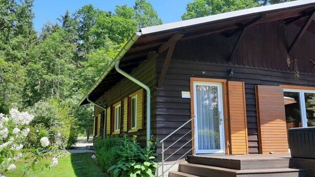 Una baita di legno con un portico coperto, una scala che conduce all'ingresso e un giardino fiorito.