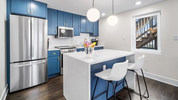 A modern kitchen with blue cabinets, stainless steel appliances, and a central island with bar stools.