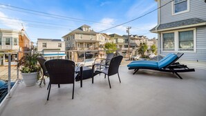A balcony with wicker chairs and a sun lounger overlooking a row of houses.