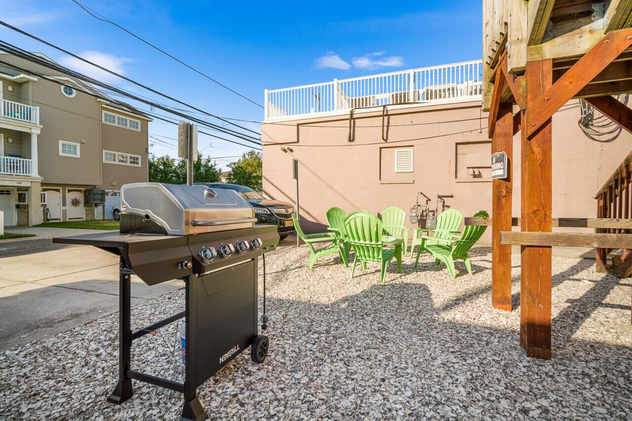 A barbecue grill with a cart, outdoor seating with green chairs, and a building with a balcony.