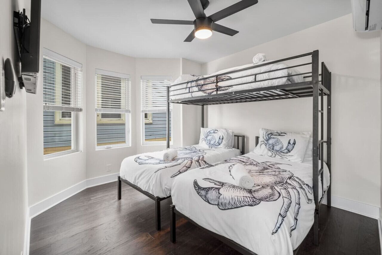 Une chambre avec un lit superposé, un ventilateur de plafond et une fenêtre avec des stores.