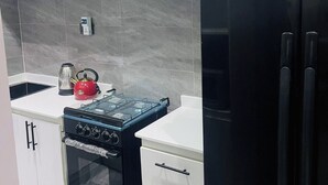 Une cuisine moderne avec des meubles blancs, une cuisinière noire, une bouilloire rouge et un réfrigérateur noir.