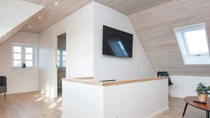 A modern, well-lit room with a wooden ceiling, a built-in desk with a flat-screen TV, a window with blinds, and a potted plant. - 6 Person Holiday Home in Sydals (Sydals)