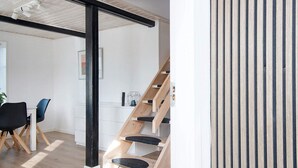 A modern interior with a wooden staircase, a dining area with chairs, and a white wall with a picture frame. - 6 Person Holiday Home in Sydals (Sydals)