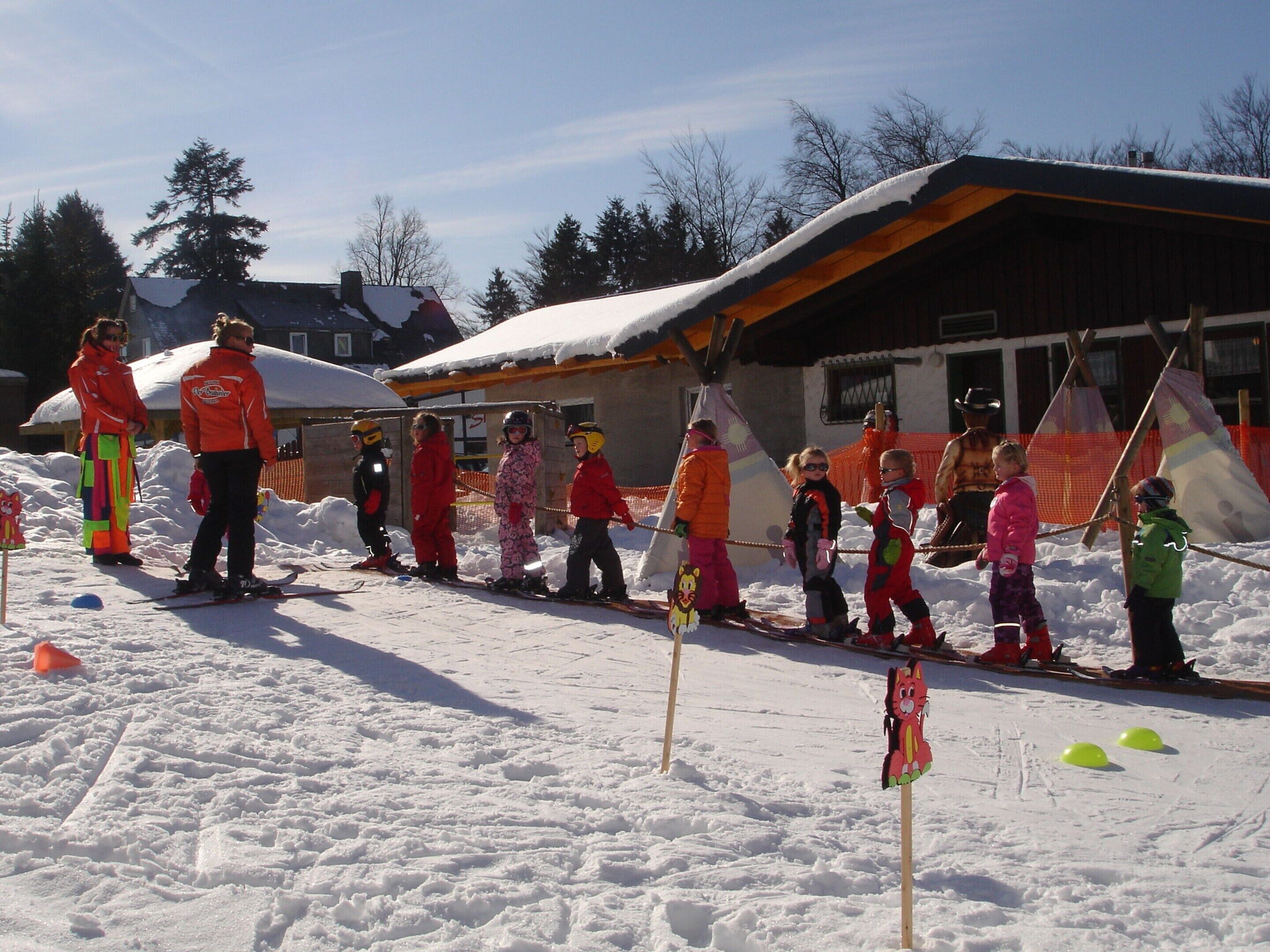 A group of children skiing in a snowy area with a building in the background.