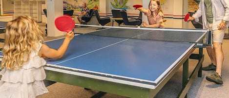 A ping pong table in a room with chairs and a mural on the wall.
