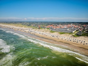 An aerial view of a coastal area with a beach lined with beach huts and a row of houses.