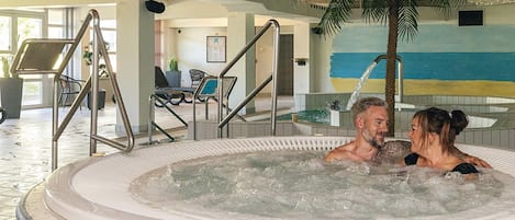 A hot tub area with a palm tree, lounge chairs, and a tiled floor.