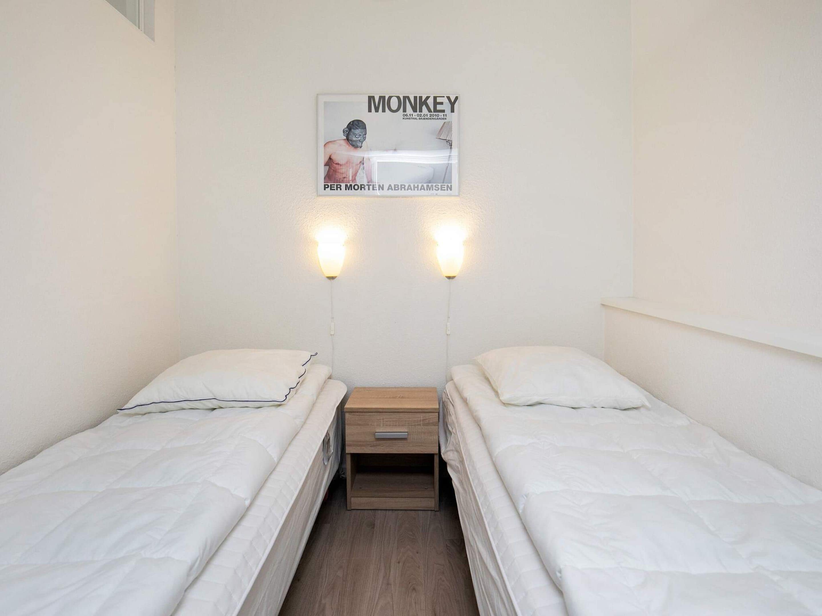 Habitació petita i ordenada amb dos llits individuals, una taula de nit de fusta i una làmpada penjada a la paret.