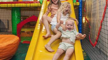 Children playing on a yellow slide in an indoor play area with a netted enclosure.