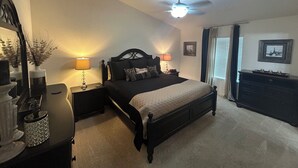 A bedroom with a bed, bedside tables, a dresser, a ceiling fan, and a window with curtains.