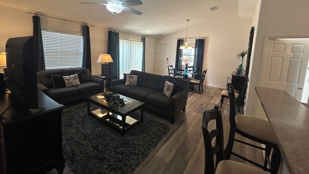 A living room with a ceiling fan, a coffee table, sofas, and a dining area with a table and chairs.