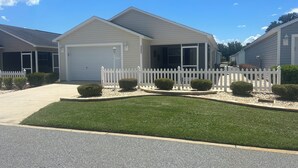 A single-story house with a white garage door, a covered porch, and a white picket fence.