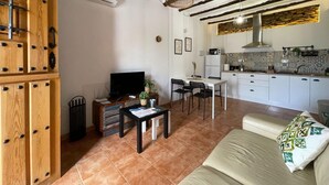 Una sala de estar con televisor, una mesa de comedor con sillas, un sofá y una cocina con microondas y estufa.
