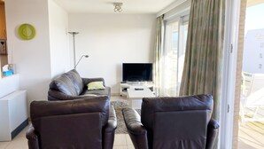 A modern living room with a sofa, two armchairs, a TV, and a large window with curtains. - Apartment Nieuwpoort Near Beach & Marina (Nieuwpoort)