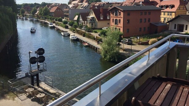 A riverside view with a dock, boats, and buildings along the water. - Holiday Apartment Amsterdam (Plau am See)