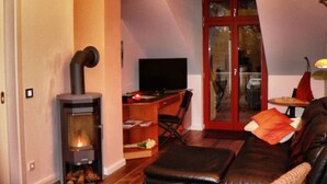 A cozy living room with a fireplace, a sofa, and a television. - Holiday Apartment Amsterdam (Plau am See)