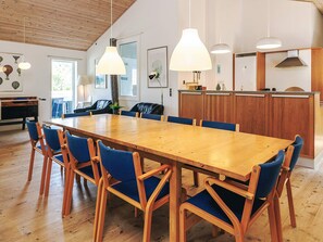 A dining area with a wooden table and blue chairs, wooden ceiling, pendant lights, and a kitchen area with wooden cabinets. - 12 Person Holiday Home in Rodby (Rodby)