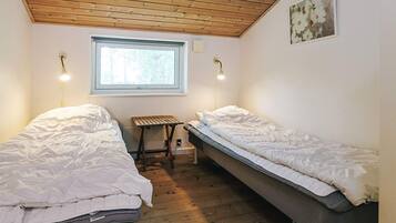 A room with two single beds, a small table, a window, and a wooden ceiling.
