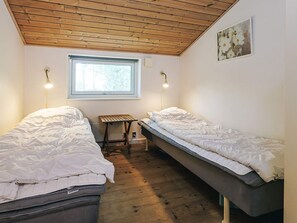 Ein Zimmer mit zwei Einzelbetten, einem kleinen Tisch, einem Fenster und einer Holzbalkendecke.