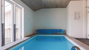 A swimming pool with clear water, a wooden ceiling, and a blue bench. - 12 Person Holiday Home in Rodby (Rodby)